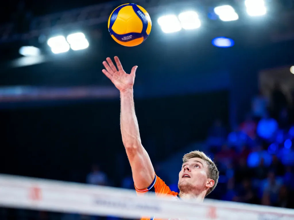 Siatkarz w wyskoku wykonujący dynamiczny atak podczas meczu w hali sportowej.